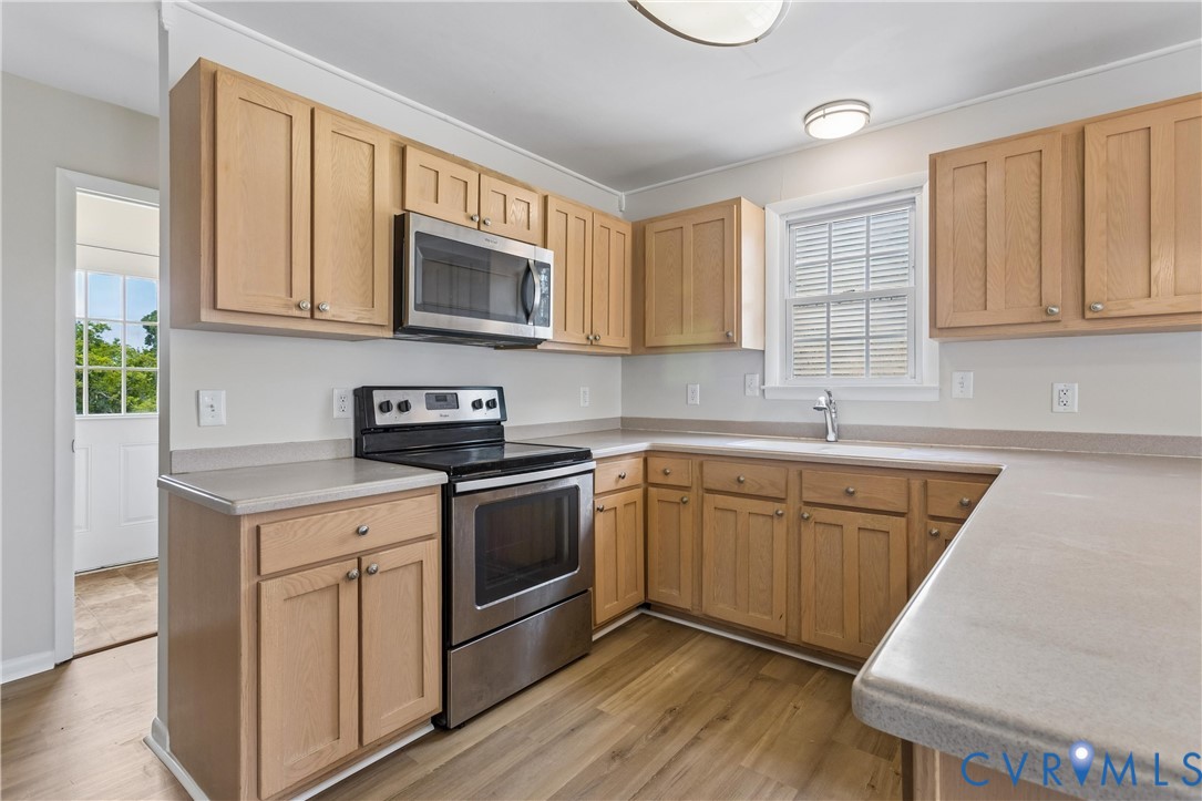 Kitchen featuring wood cabinetry, stainless steel appliances, solid-surface countertops, and wood-finish flooring