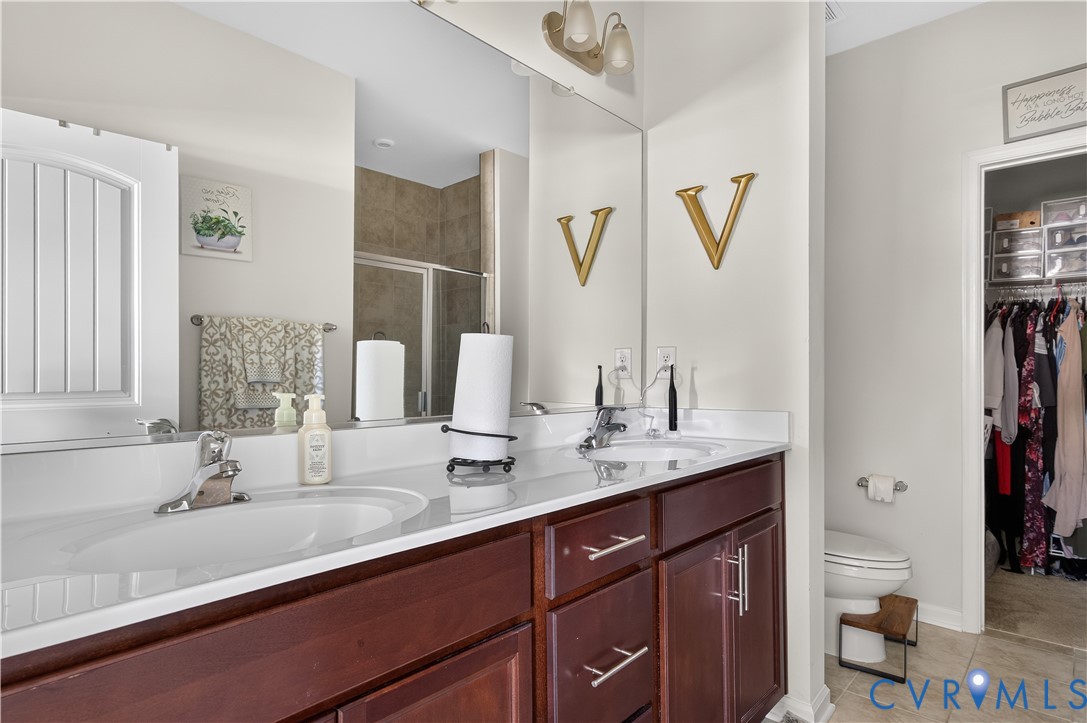 Dual-sink vanity with dark wood-finish cabinetry, solid-surface countertop, full-width mirror, and chrome-finish hardware