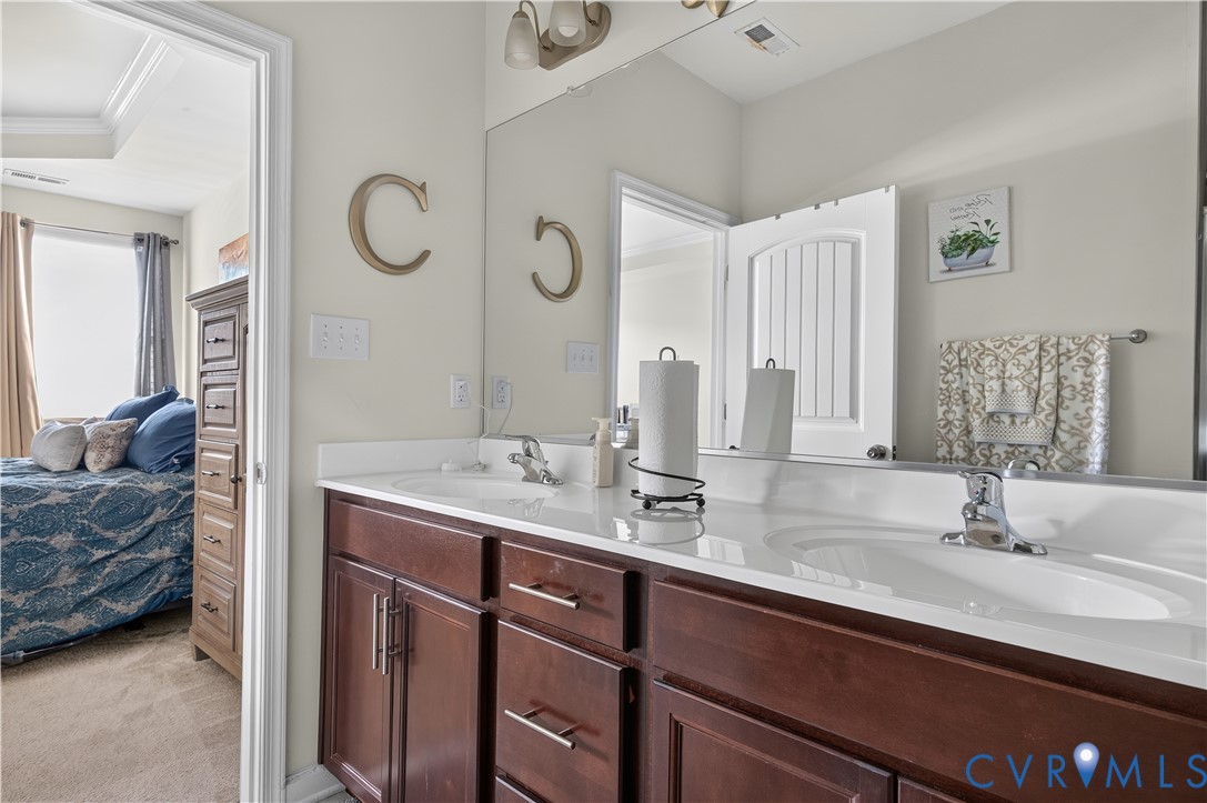 Double vanity featuring dark wood-finish cabinetry, integrated white countertops with dual drop-in sinks, polished chrome faucets, and an expansive wall-mounted mirror