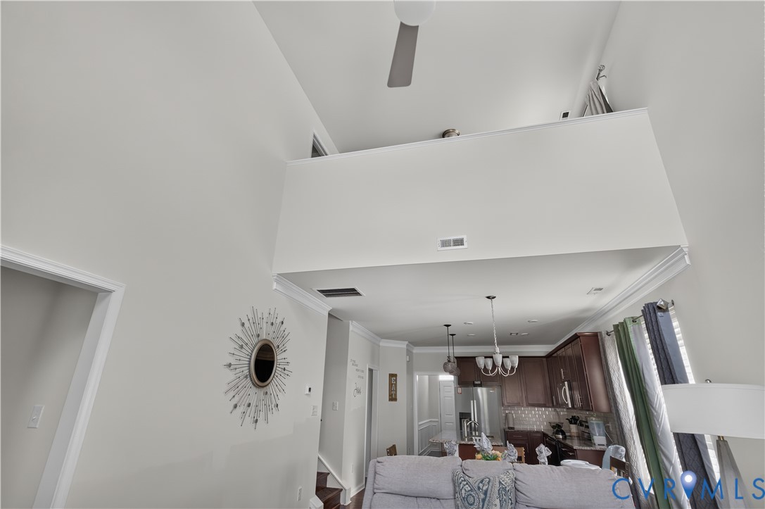 Vaulted ceilings, mezzanine overlook, stainless steel refrigerator, dark wood cabinetry, and crown molding