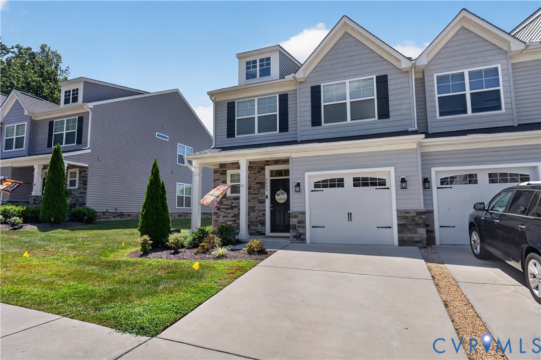 Multi-level exterior featuring light gray horizontal siding, stone veneer accents, double-gable roofline, and two attached garages