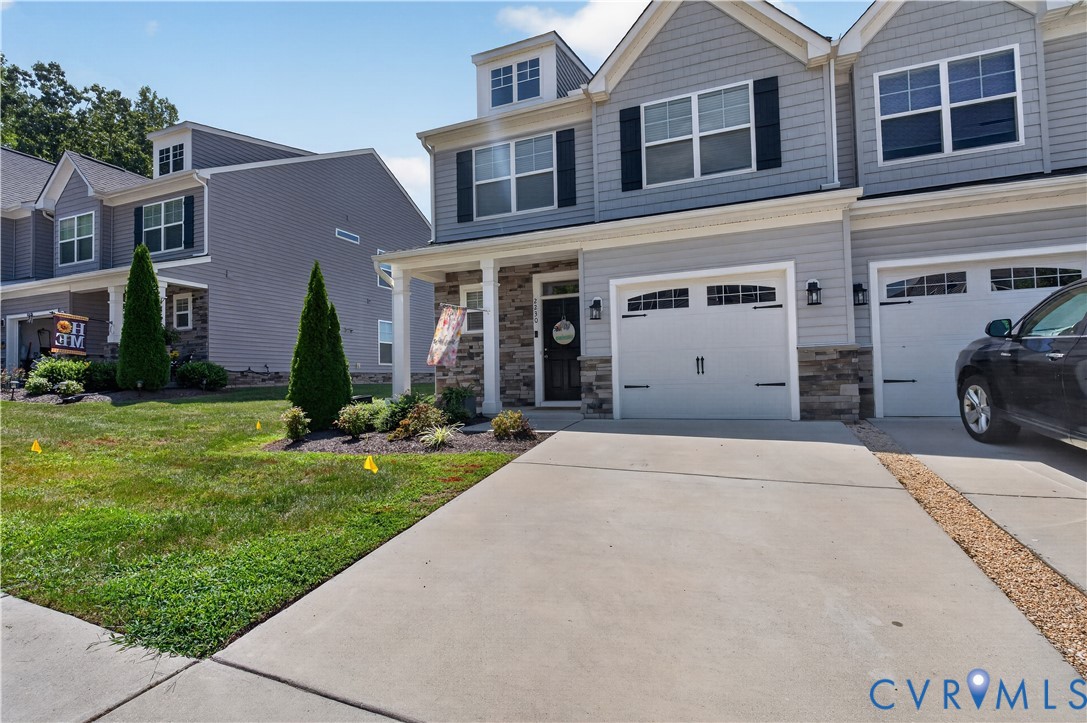 Multi-level townhome featuring horizontal lap siding, stone veneer accents, multi-pane windows with dark shutters, and attached two-car garages with arched-top detailing