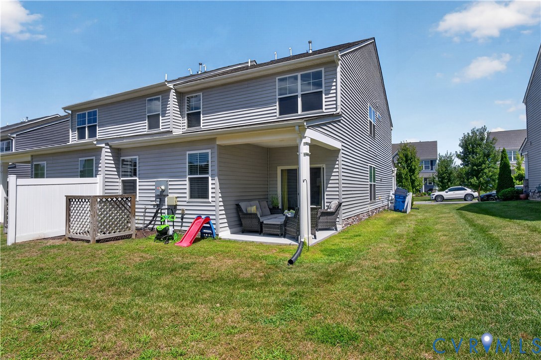 Multi-level residence featuring horizontal vinyl siding, a covered concrete patio, and a white privacy fence enclosing a portion of the yard