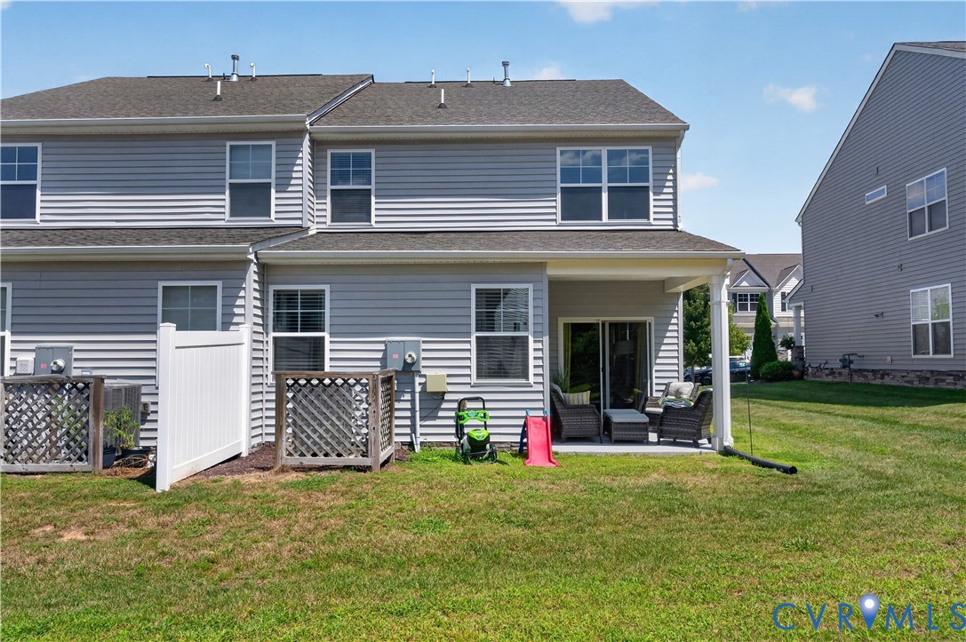 Gray vinyl siding exterior featuring a covered rear patio, white vinyl privacy fencing, and lattice-enclosed mechanical units