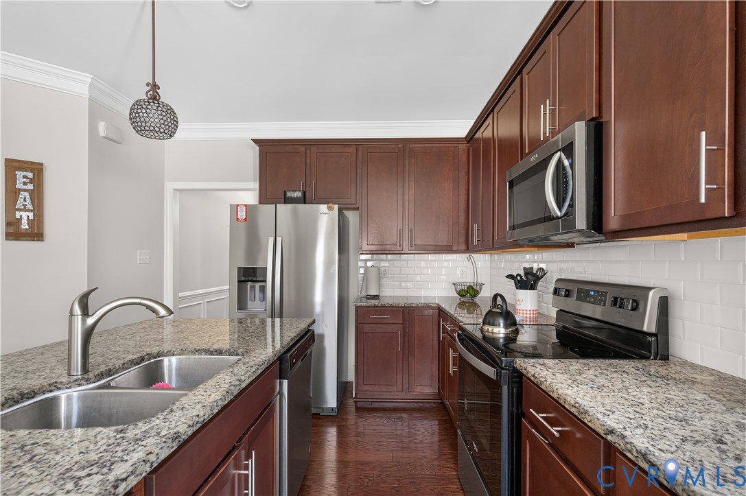 Kitchen featuring stained wood cabinetry, stone countertops, white subway tile backsplash, stainless steel appliances, and wood-finish flooring
