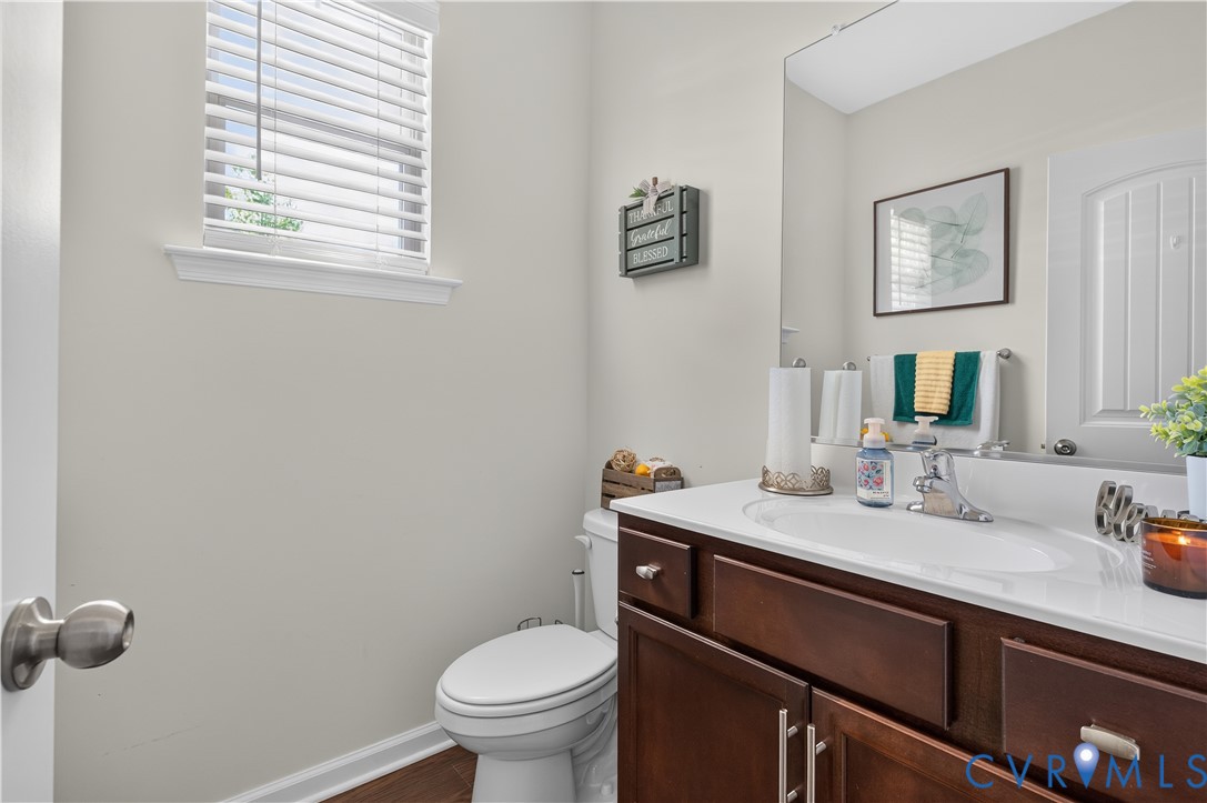 Bathroom featuring a dark wood-finish vanity, solid-surface countertop with an integrated basin, wall-mounted mirror, and wood-finish flooring