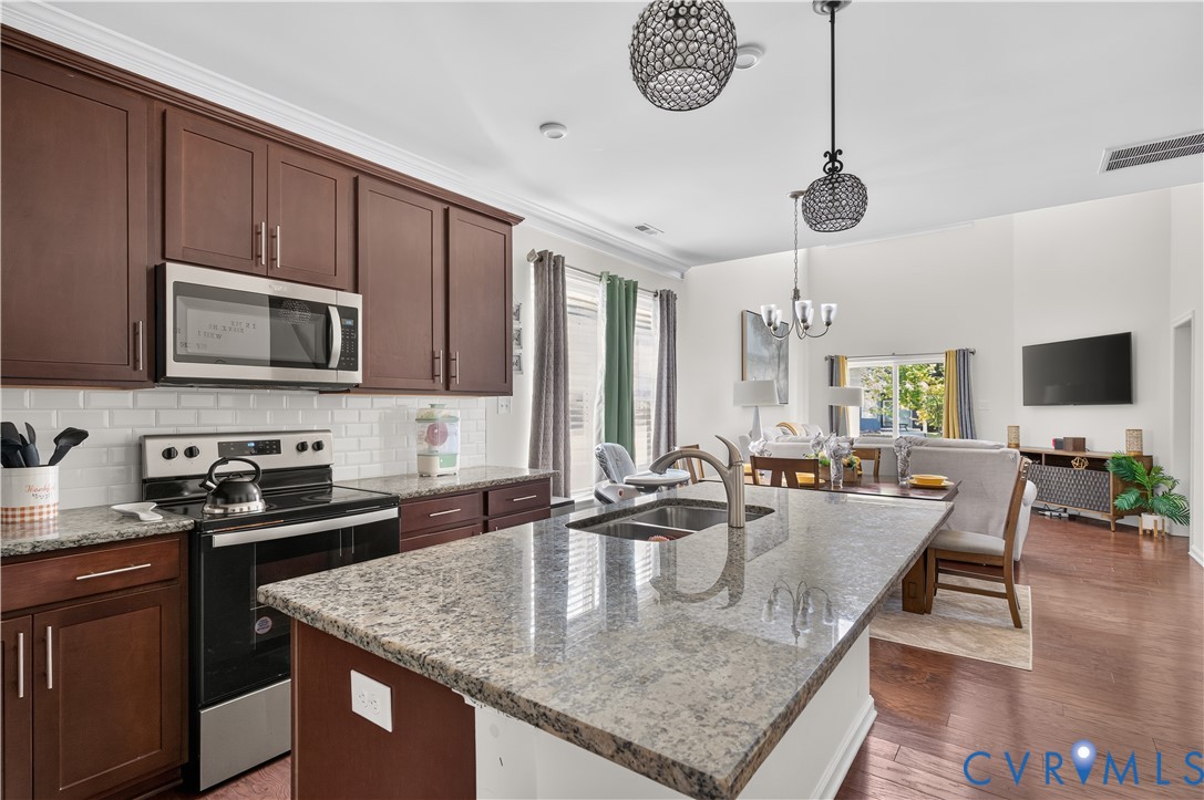 Kitchen featuring dark-finish cabinetry, stone countertops, stainless steel appliances, subway tile backsplash, and wood-finish flooring