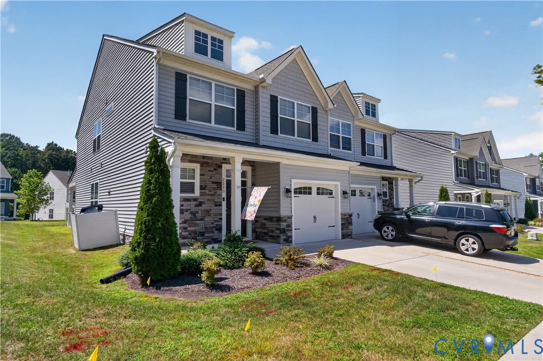 Multi-level residence featuring gray vinyl siding, stone veneer accents, dormer windows, and a double-bay garage with carriage-style doors
