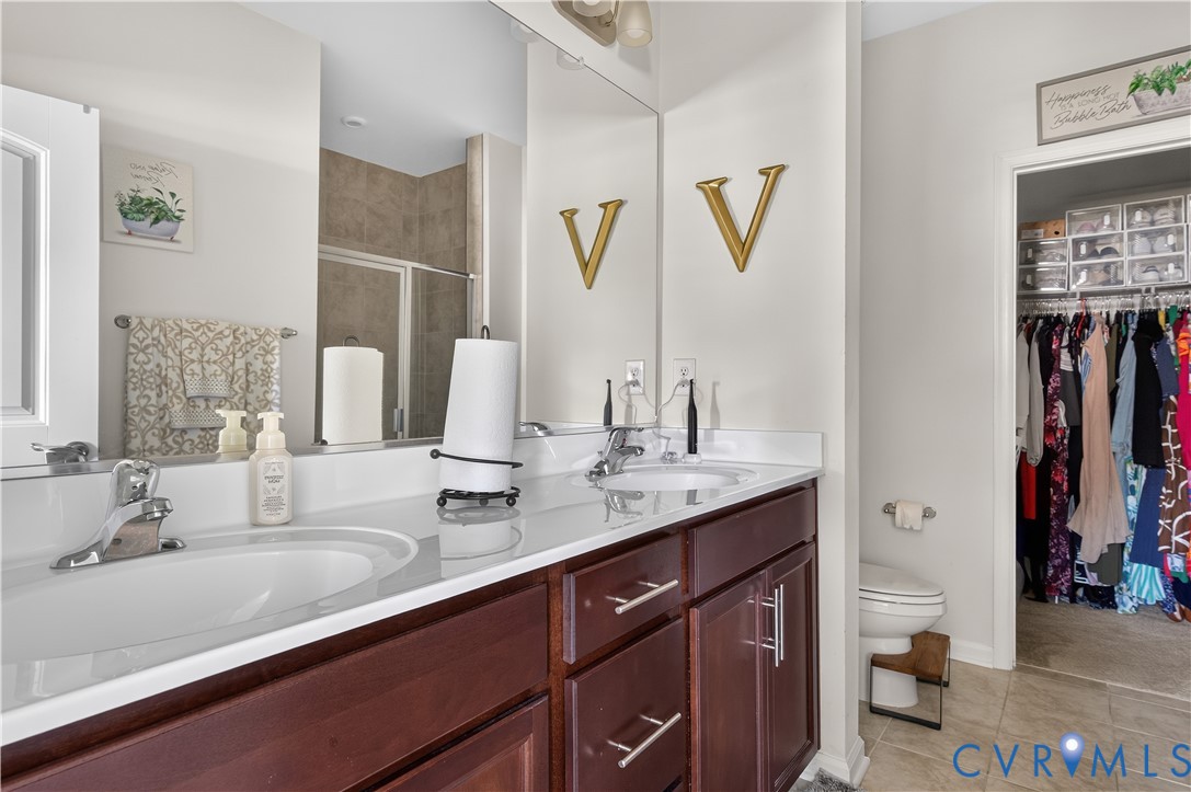 Double vanity featuring dark wood cabinetry, a light-toned countertop, dual inset sinks, polished chrome hardware, and an expansive wall-mounted mirror