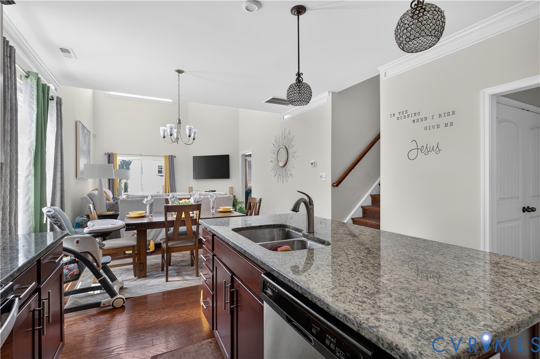 Kitchen featuring stone countertops, dark wood cabinetry, double-basin stainless steel sink, pendant lighting, and wood-finish flooring
