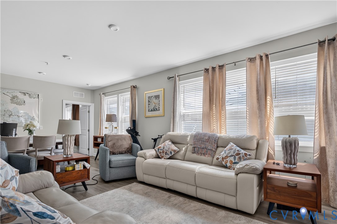 Open-concept living space featuring wood-finish flooring and expansive windows with horizontal blinds