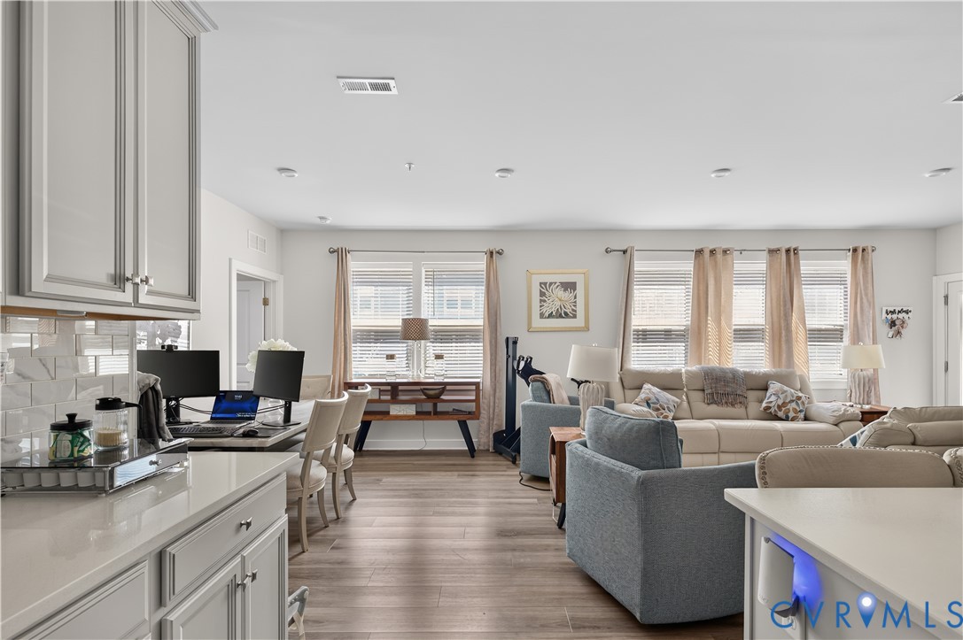 Kitchen featuring gray cabinetry, light-toned countertops, and a subway tile backsplash, complemented by wood-finish flooring and multiple windows