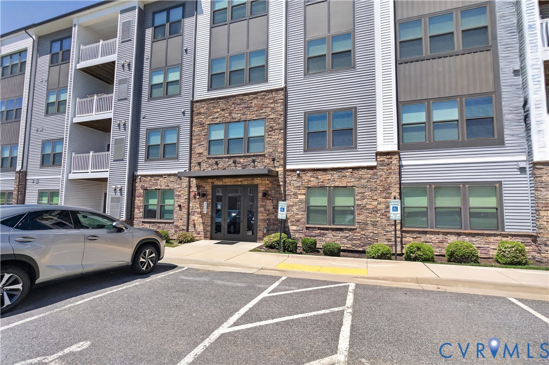 Multi-story building exterior featuring stone masonry cladding, horizontal siding, private balconies with white railings, and an entry canopy