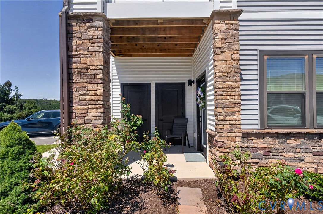 Exterior entry featuring stone veneer columns, horizontal siding, two dark-toned doors, and a covered concrete patio