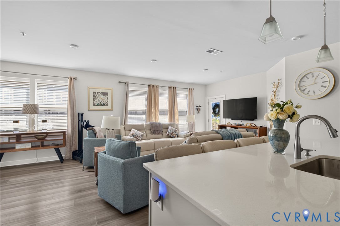 Open-concept interior featuring wood-finish flooring, recessed lighting, and a kitchen island with stone-surface countertop and undermount stainless steel sink