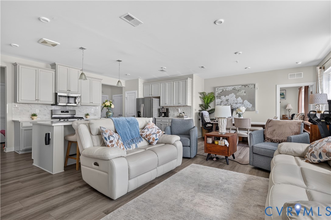 Kitchen featuring light-toned cabinetry, stainless steel appliances, a peninsula with bar seating, and stone-finish backsplash, accented by wood-finish flooring