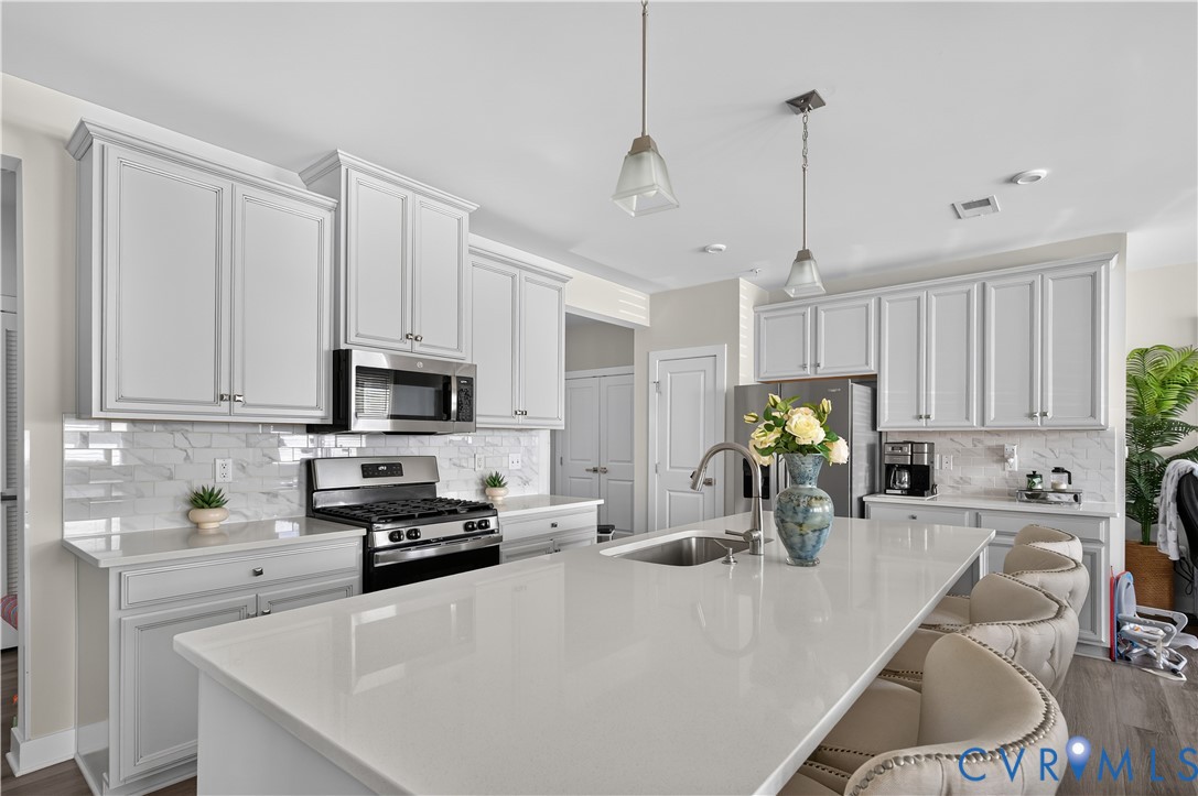 Kitchen featuring shaker-style cabinetry, quartz countertops, a tile backsplash, a center island with an undermount stainless steel sink, and stainless steel appliances