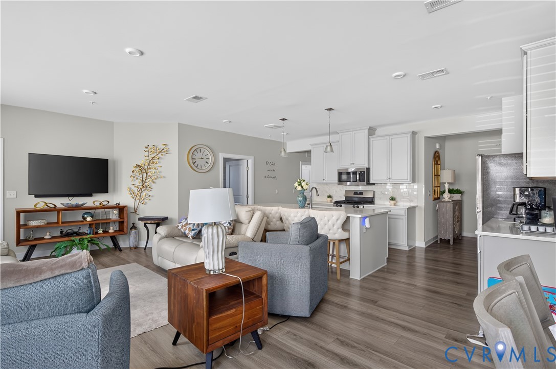 Open-concept interior featuring wood-finish flooring, recessed lighting, and a kitchen equipped with white cabinetry, a central island, and stone-finish countertops