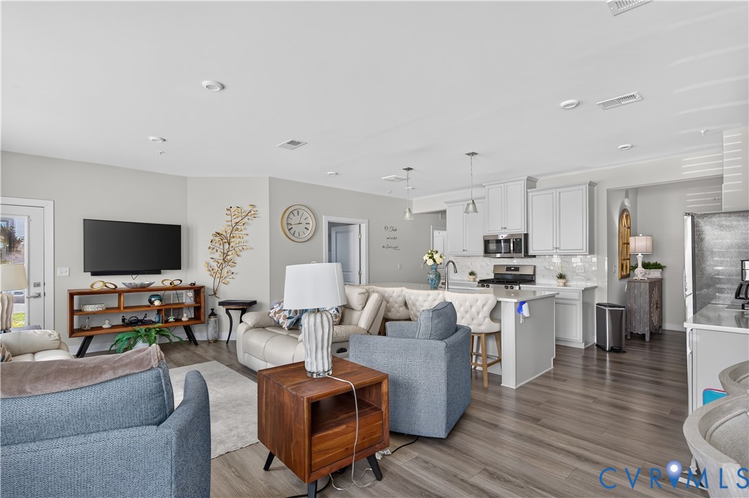 Open-concept floor plan featuring wood-finish flooring, white shaker-style cabinetry, a central kitchen island with bar seating, and recessed ceiling lighting
