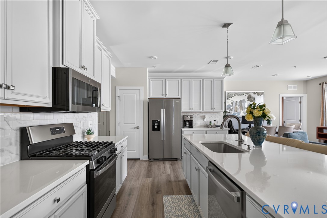 Kitchen featuring white shaker-style cabinetry, quartz countertops, subway tile backsplash, stainless steel appliances, and wood-finish flooring