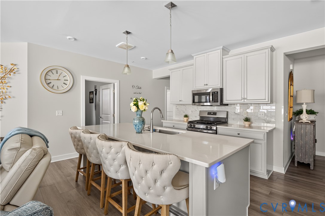 Kitchen featuring a center island with quartz countertop and undermount sink, shaker-style cabinetry, stainless steel appliances, subway tile backsplash, and wood-finish flooring