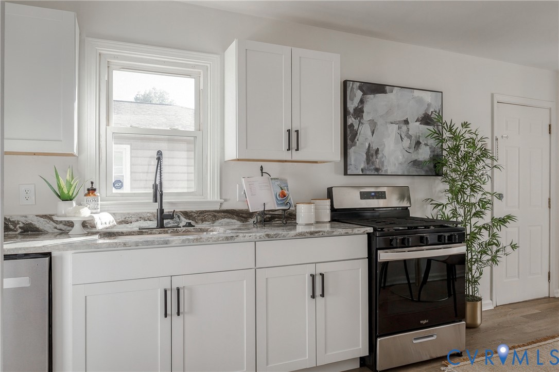 Kitchen featuring white Shaker-style cabinetry, matte black hardware, stone-patterned countertops, a high-arc faucet, and a stainless steel range