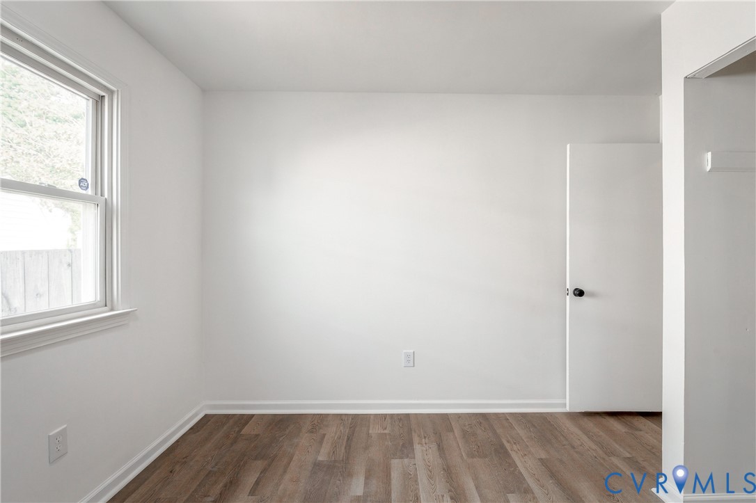 Neutral interior space featuring wood-finish flooring, crisp white walls, a single-hung window, and a paneled interior door with a round knob