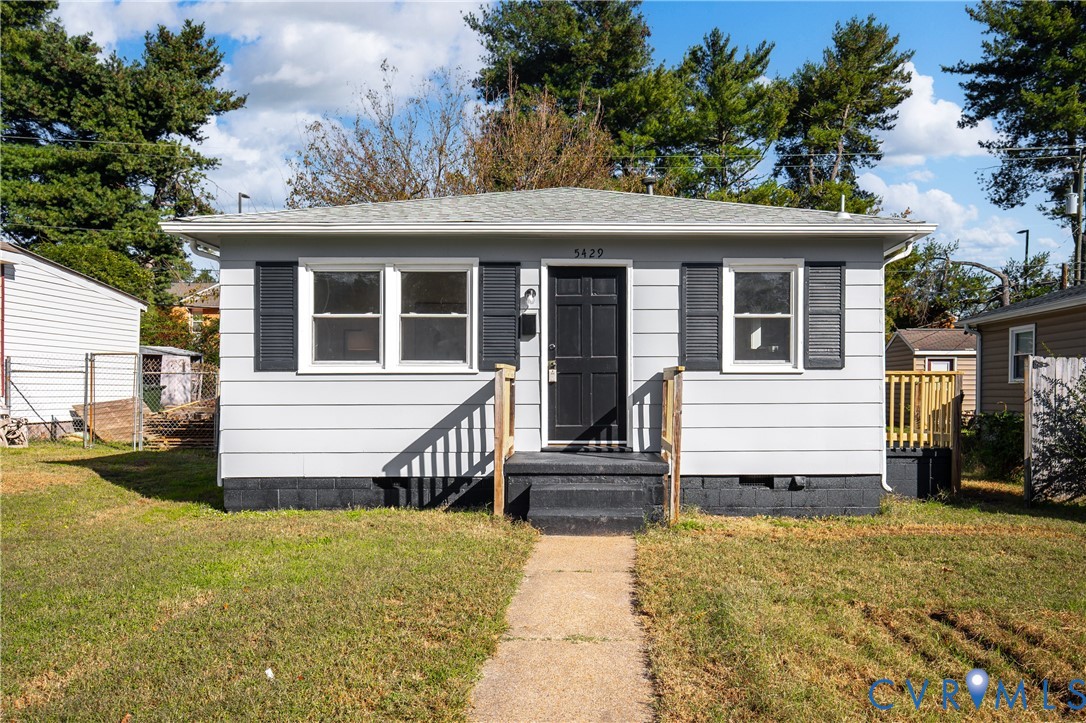 Single-story exterior featuring light gray horizontal siding, dark decorative shutters, a six-panel entry door, and a concrete pathway Single-story exterior featuring light gray horizontal siding, dark decorative shutters, a six-panel entry door, and a concrete pathway