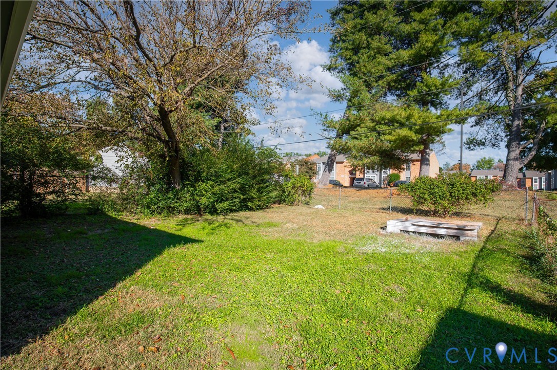 Open backyard featuring a grassy lawn, mature trees, and chain-link perimeter fencing
