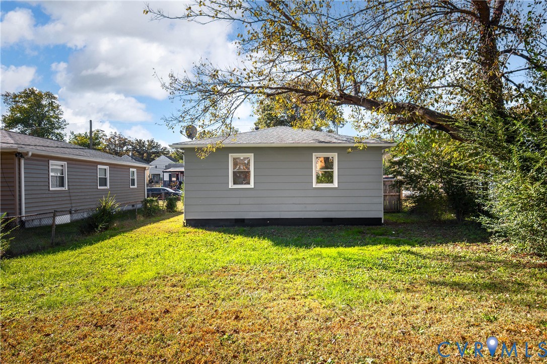 Exterior featuring grey horizontal siding, a hipped roof, and dual white-framed windows, set on a grass-covered lot with mature trees