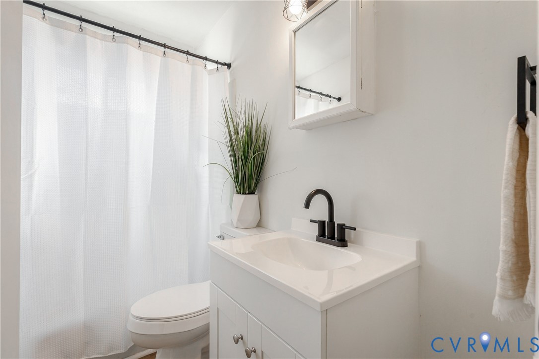 White vanity with an integrated basin, matte black faucet, mirrored medicine cabinet, and shower curtain with a black rod