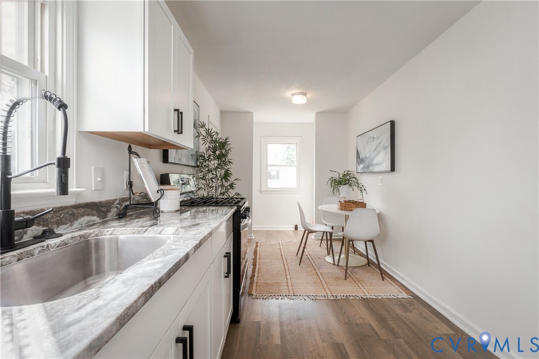 Kitchen featuring white shaker cabinetry, stone-patterned countertops, undermount stainless steel sink, matte black faucet hardware, and wood-finish flooring