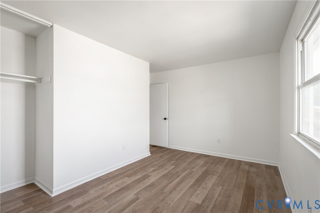Interior space featuring wood-finish flooring, white walls, a built-in closet with shelving, and a dual-pane window