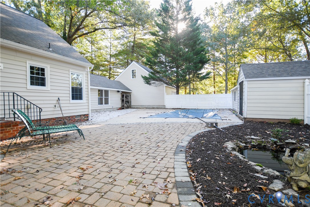 Rear exterior featuring a brick-paver patio, swimming pool with cover, detached outbuilding, and stone-lined garden pond