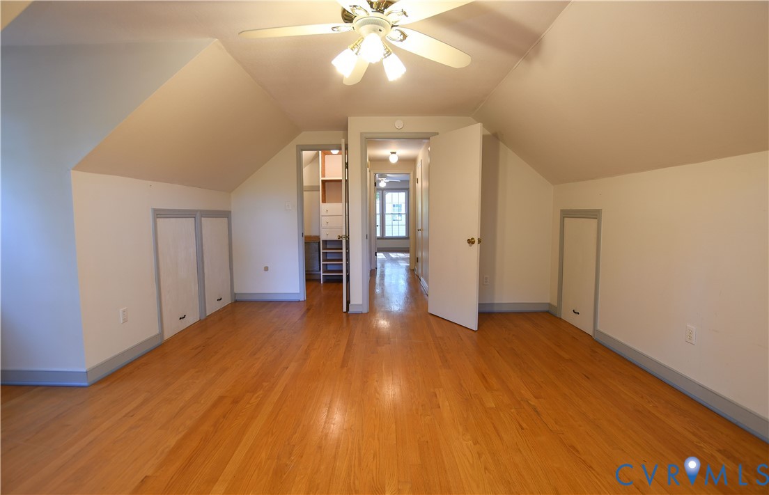 Vaulted ceilings featuring wood-finish flooring, built-in knee-wall storage, and a ceiling-mounted light fixture