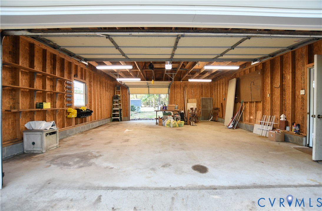 Attached garage featuring exposed wood stud construction, concrete flooring, built-in wall shelving, and linear overhead lighting