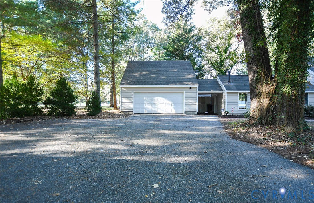 Attached garage with horizontal siding, shingled roof, asphalt driveway, and wooded grounds