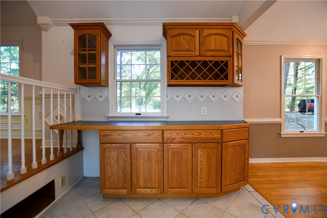 Custom wood cabinetry with integrated wine rack, dark countertop, ceramic tile flooring, and white spindle railing