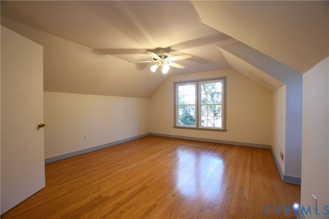 Room featuring wood-finish flooring, vaulted ceilings, dual-pane window with trim, and a multi-light ceiling fan