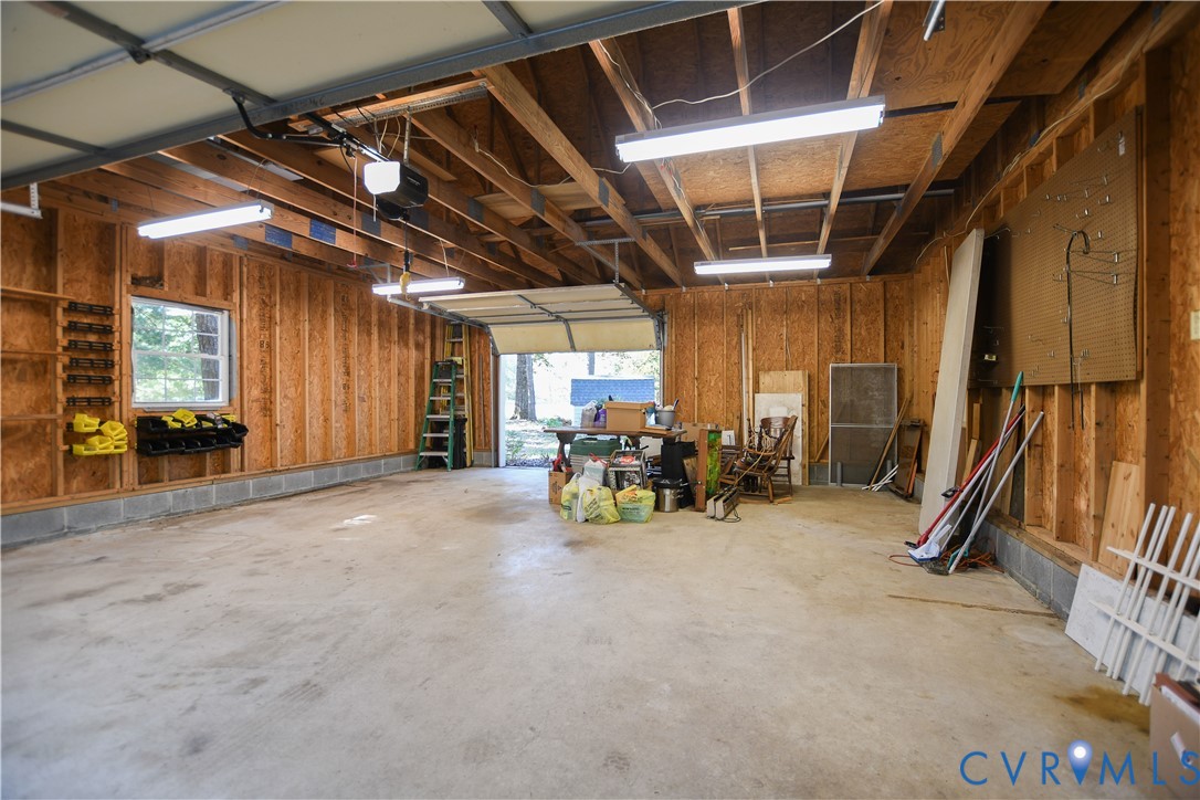 Multi-car garage featuring exposed wood-stud walls, concrete flooring, linear fluorescent lighting, and built-in wall storage shelving