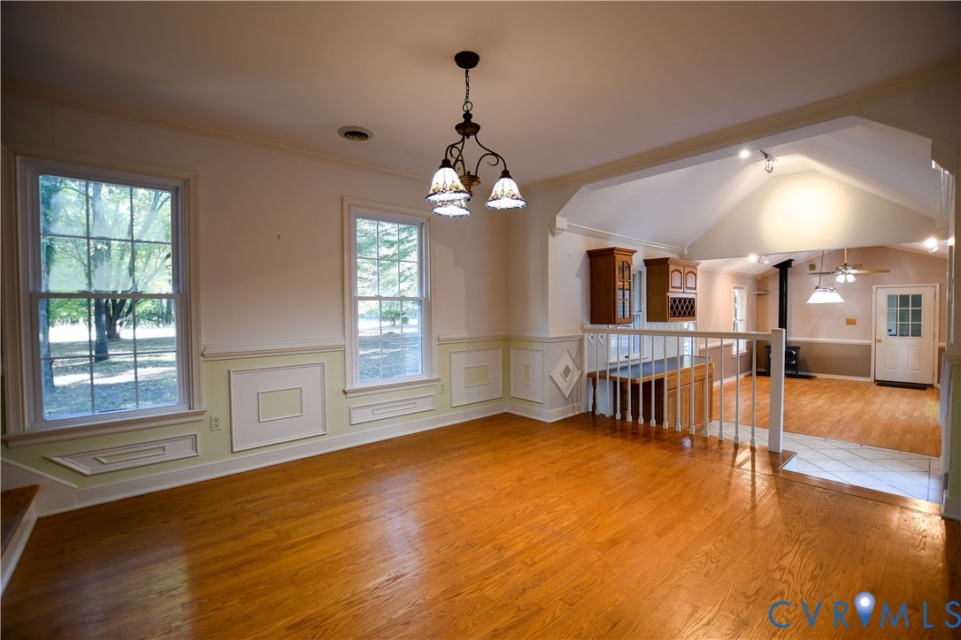 Wood-finish flooring, wainscoting with decorative millwork, multi-pane windows, vaulted ceiling, and built-in cabinetry with glass-front display