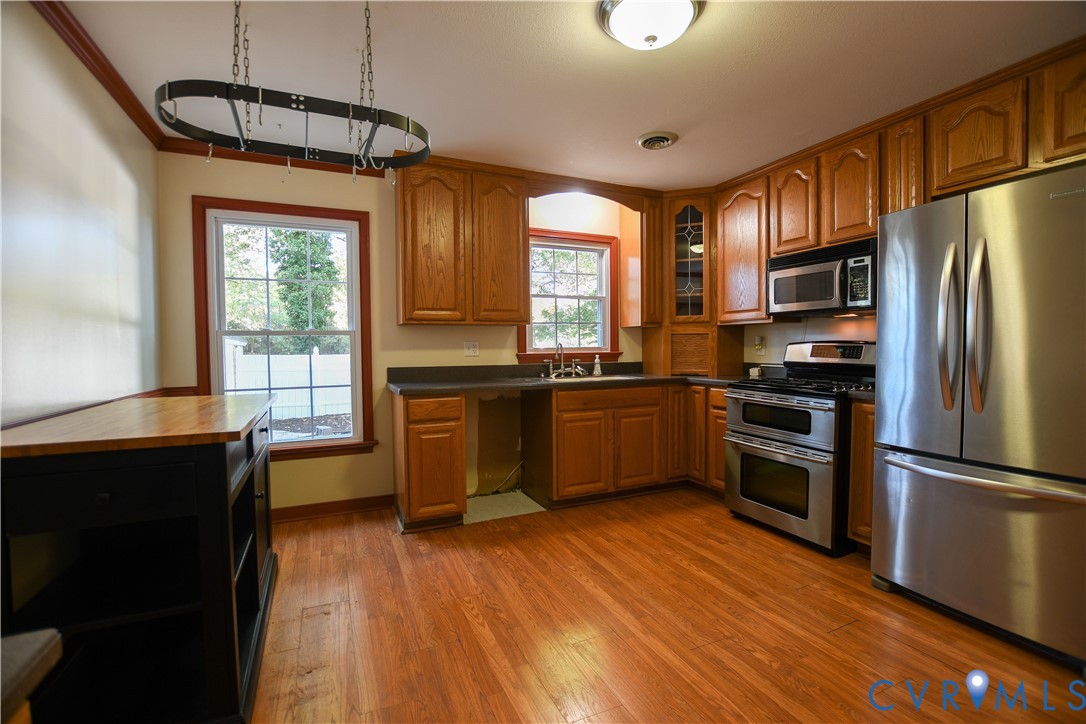 Kitchen featuring wood cabinetry, stainless steel appliances, dark countertops, wood-finish flooring, and multi-pane windows