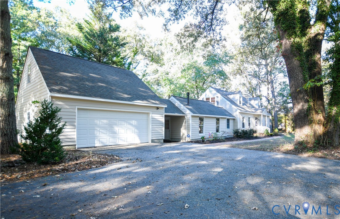 Exterior facade featuring horizontal siding, a two-car garage, and an expansive gravel driveway situated amidst mature trees