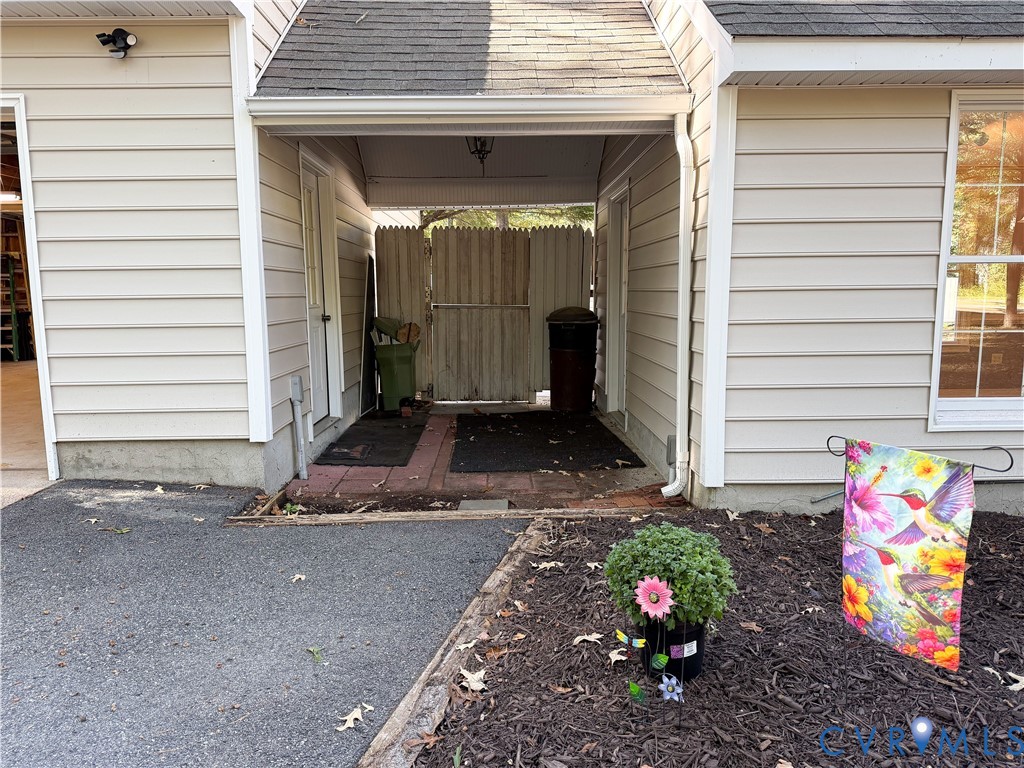 Covered entryway featuring horizontal vinyl siding, a brick-paver threshold, and a full-height privacy fence