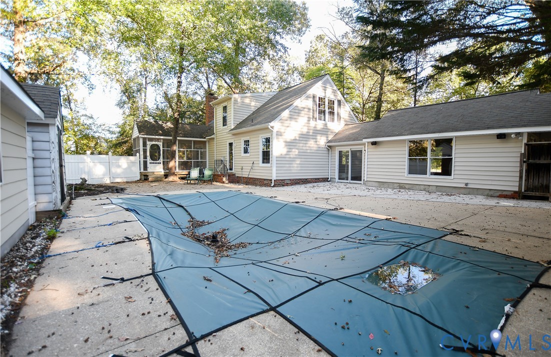 Exterior featuring a swimming pool with a safety cover, expansive concrete patio, screened porch, vinyl siding, and mature tree-lined perimeter