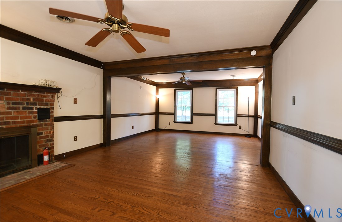 Hardwood flooring, brick fireplace, dark-stained crown molding and chair rail trim, and dual ceiling fans
