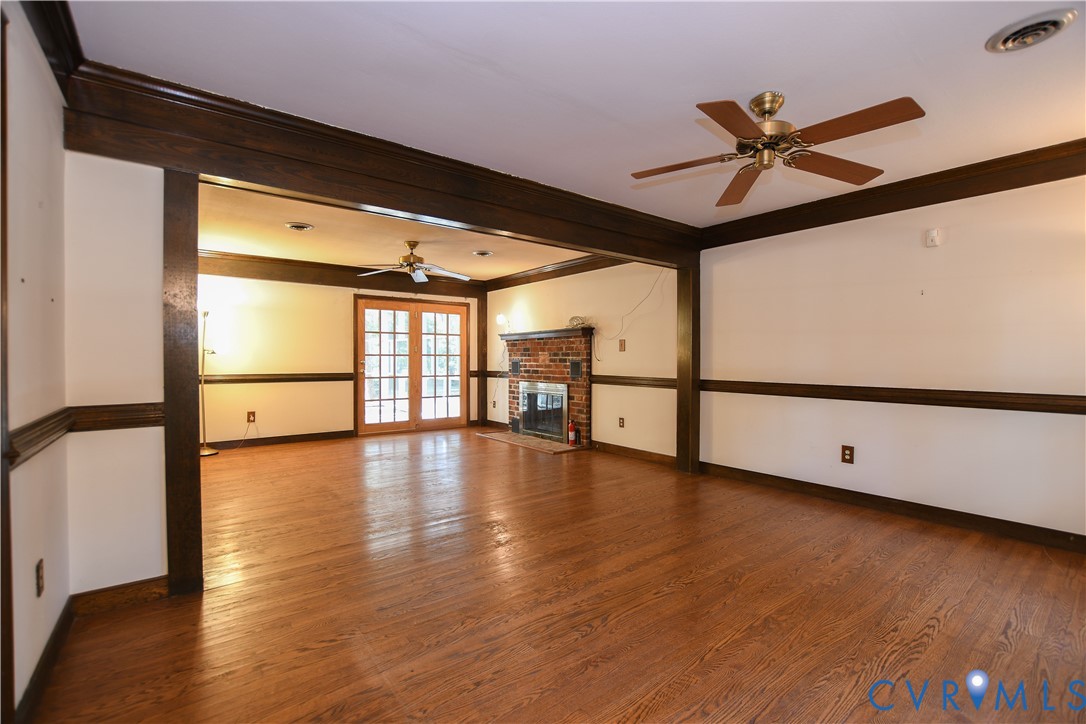Spacious interior featuring wood-finish flooring, dark wood-tone crown molding and chair rail, brick fireplace, and French-style glass doors