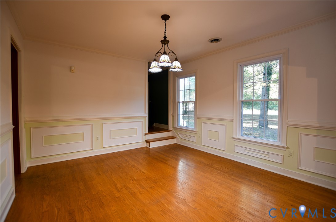 Room featuring wood-finish flooring, wainscoting, multi-pane windows, and a hanging light fixture