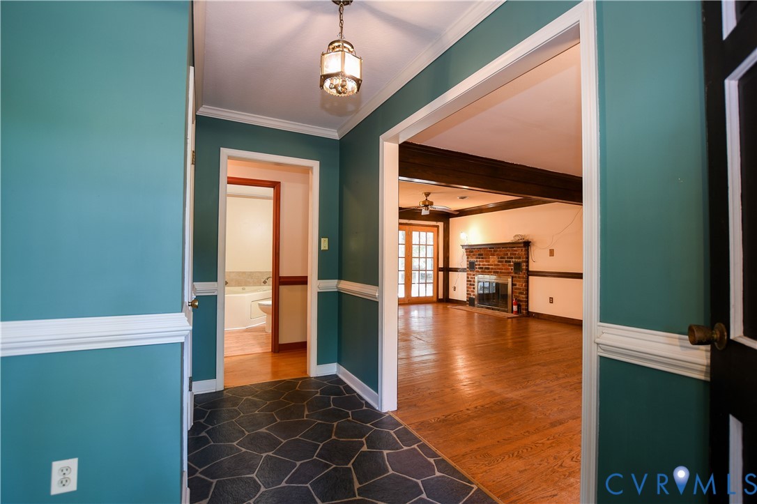 Foyer featuring flagstone flooring, chair rail molding, and a pendant light fixture, with hardwood flooring and a brick fireplace visible in the interior space