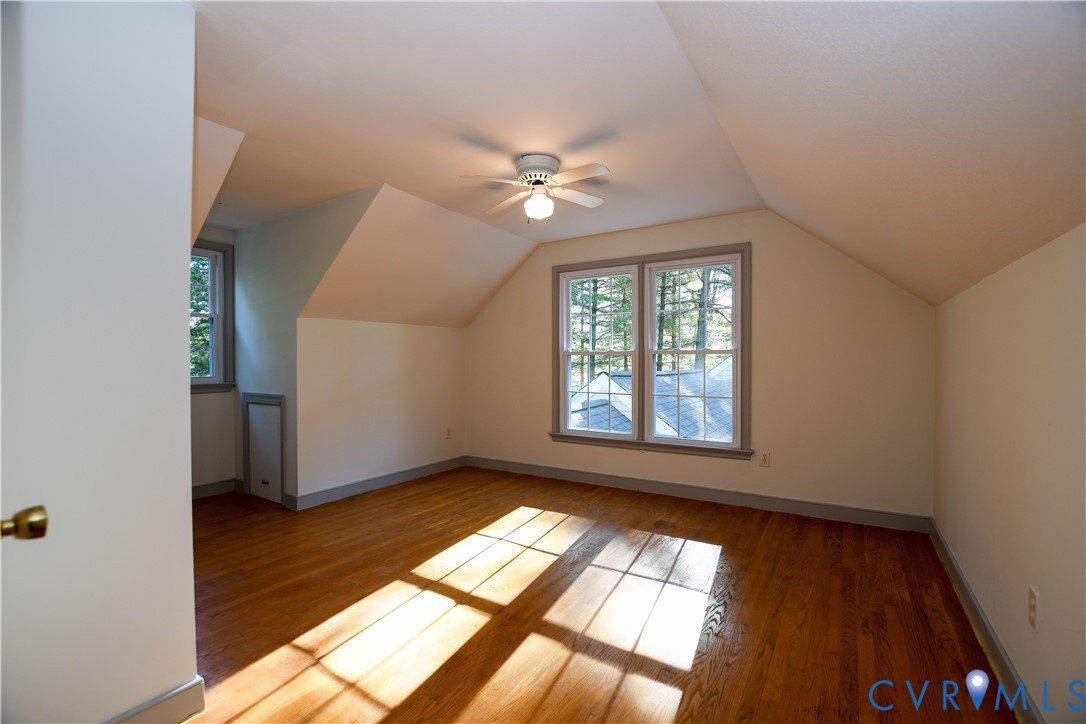 Room featuring sloped ceilings, wood-finish flooring, a ceiling fan, and double-pane windows